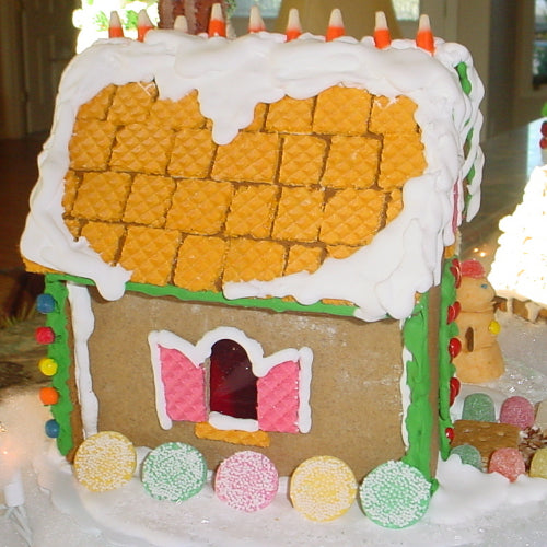 Gingerbread house with a yellow roof and colorful decorations on a table.