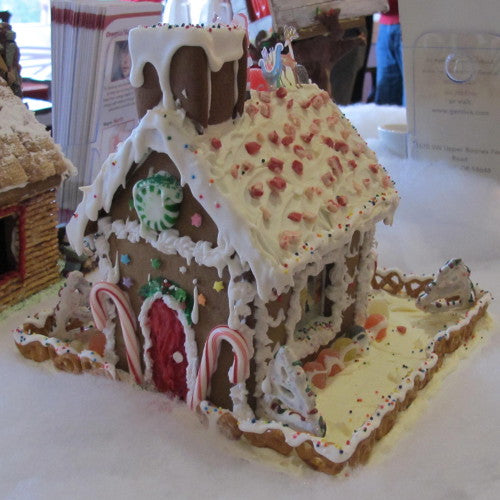 Decorative gingerbread house with white icing and candy decorations on a white surface.