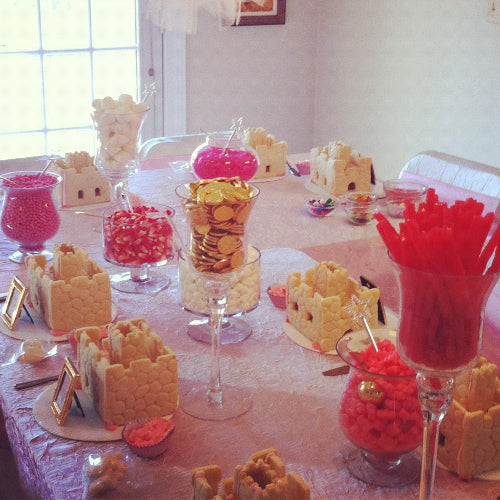 Decorative table setting with candy and cookies on a light pink tablecloth.