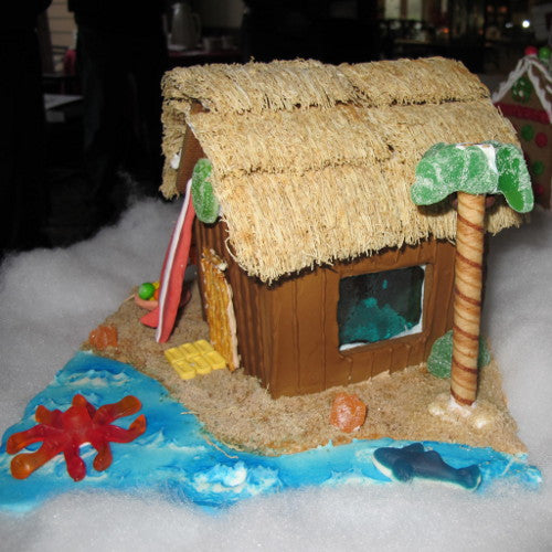 Gingerbread house shaped like a tropical hut with a thatched roof on a sandy base with ocean elements.