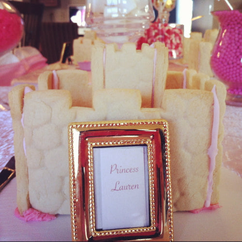 Decorative castle made of cookies with a gold frame and 'Princess Lauren' sign on a table.