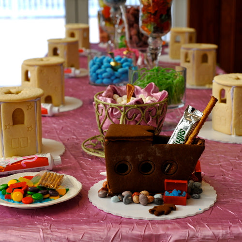 Decorative table setting with gingerbread houses and a ship cake on a pink tablecloth.