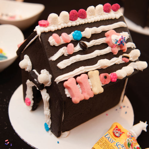 Decorative cake shaped like a house with colorful icing on a white plate.
