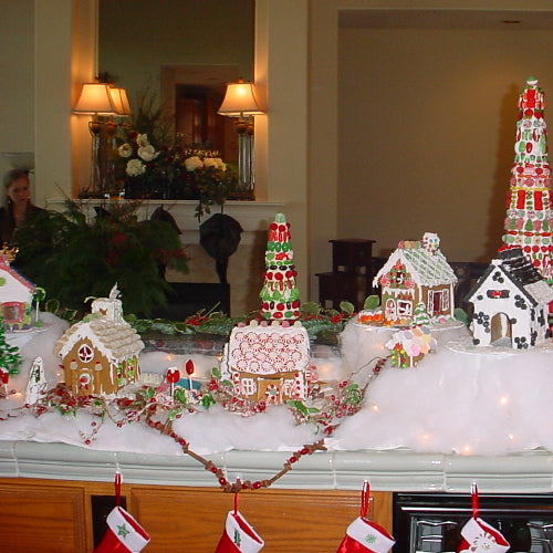 Gingerbread house display on a table with decorative lights and flowers in the background.