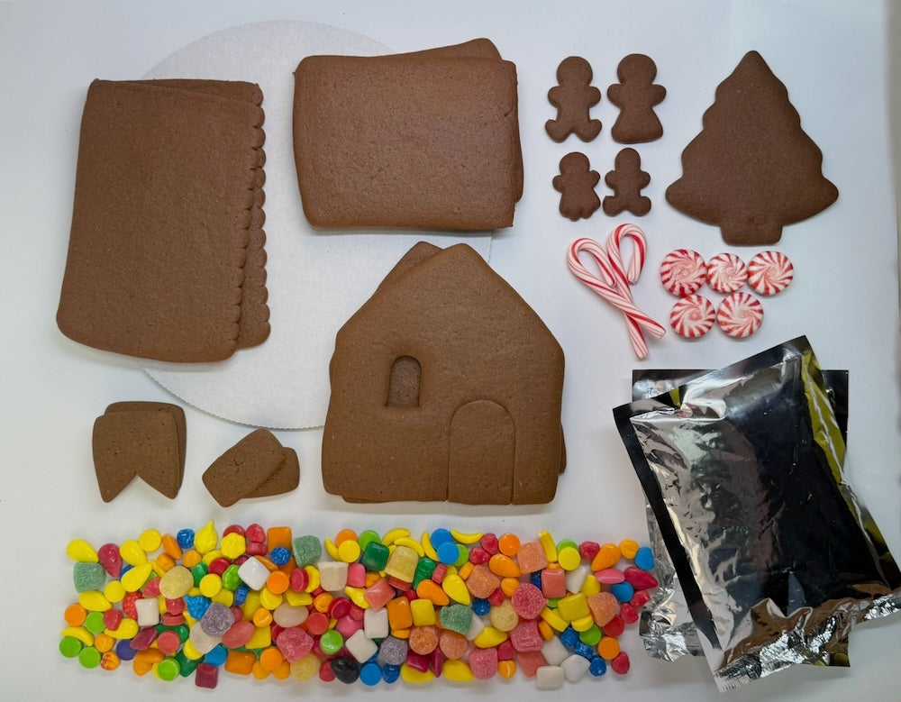 Gingerbread house kit with cookies, candy, and supplies on a white surface