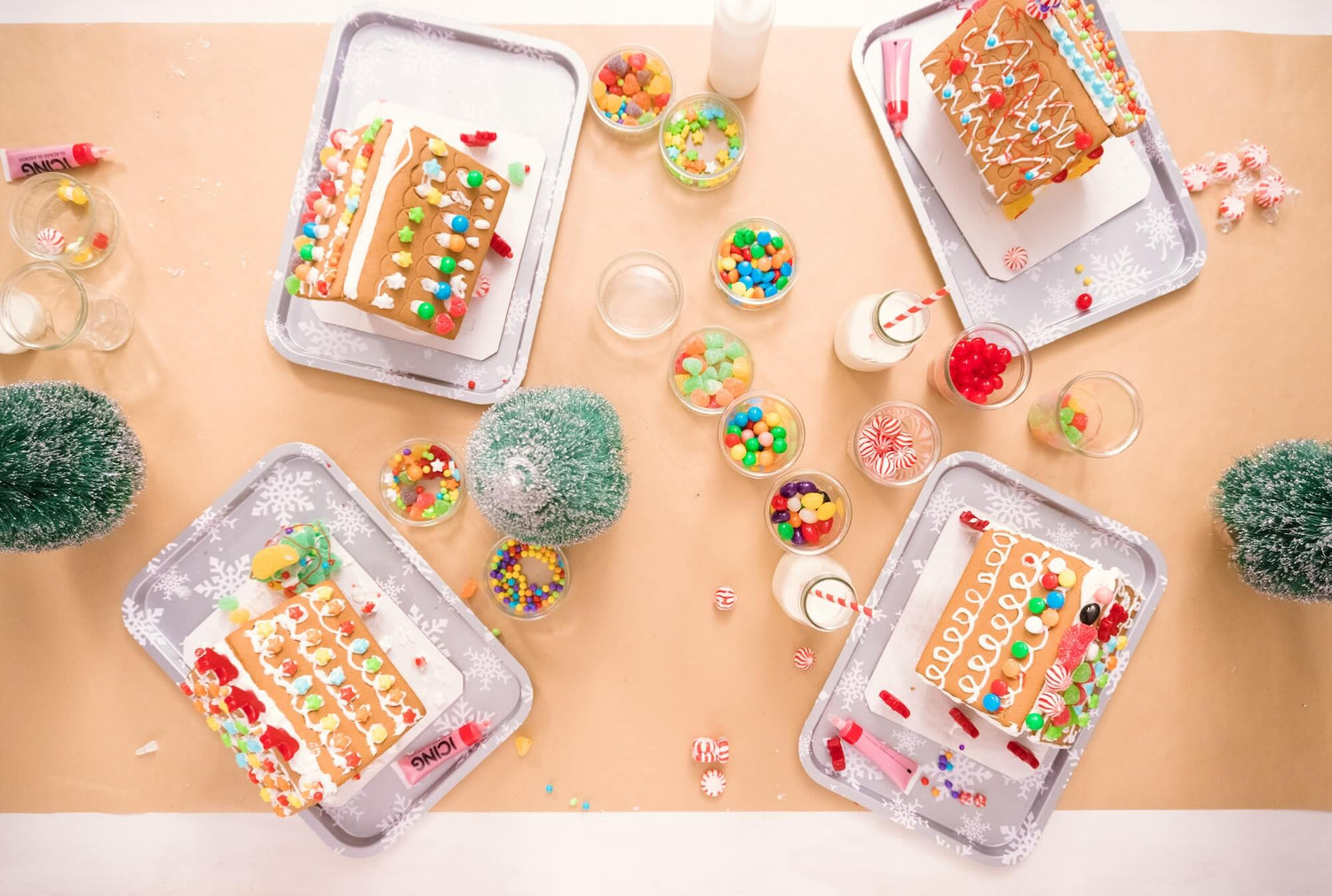 Decorative trays with gingerbread houses and candy on a beige surface