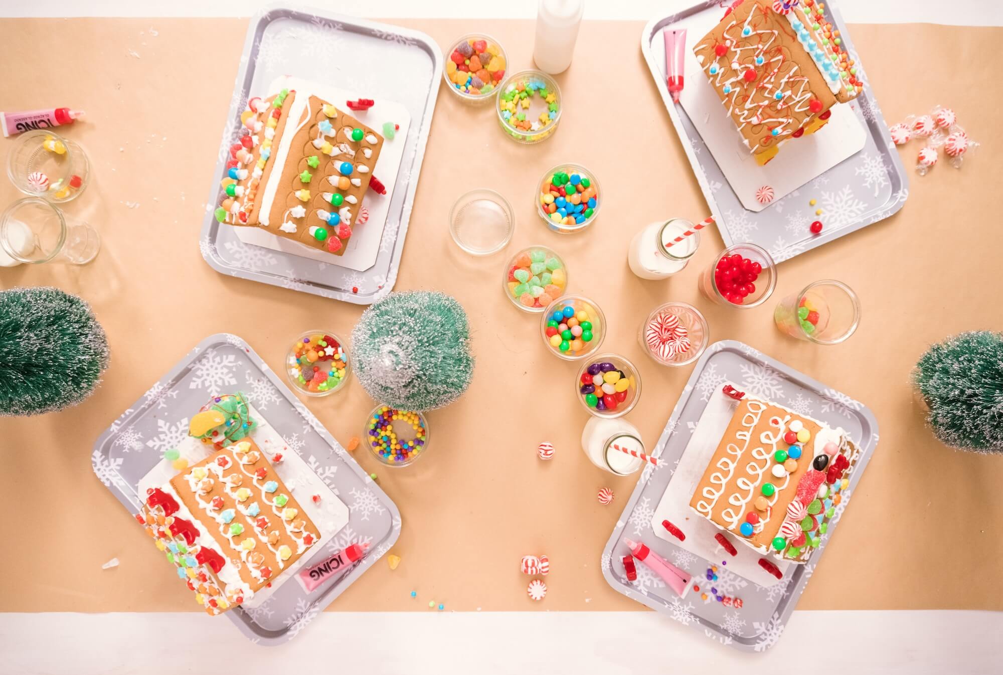 Decorative trays with gingerbread houses and candy on a beige surface