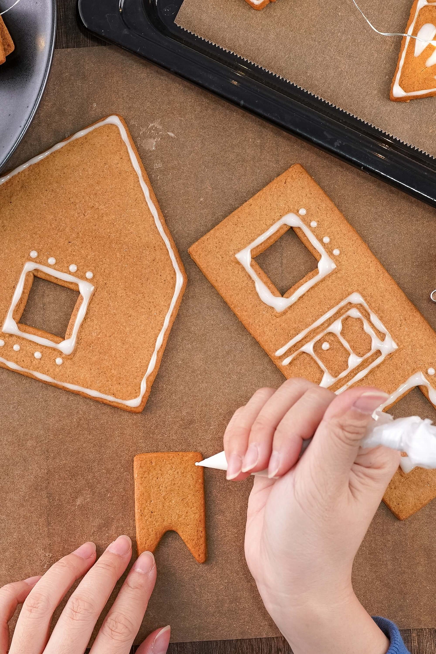 Decorating gingerbread cookies shaped like houses on a baking sheet.