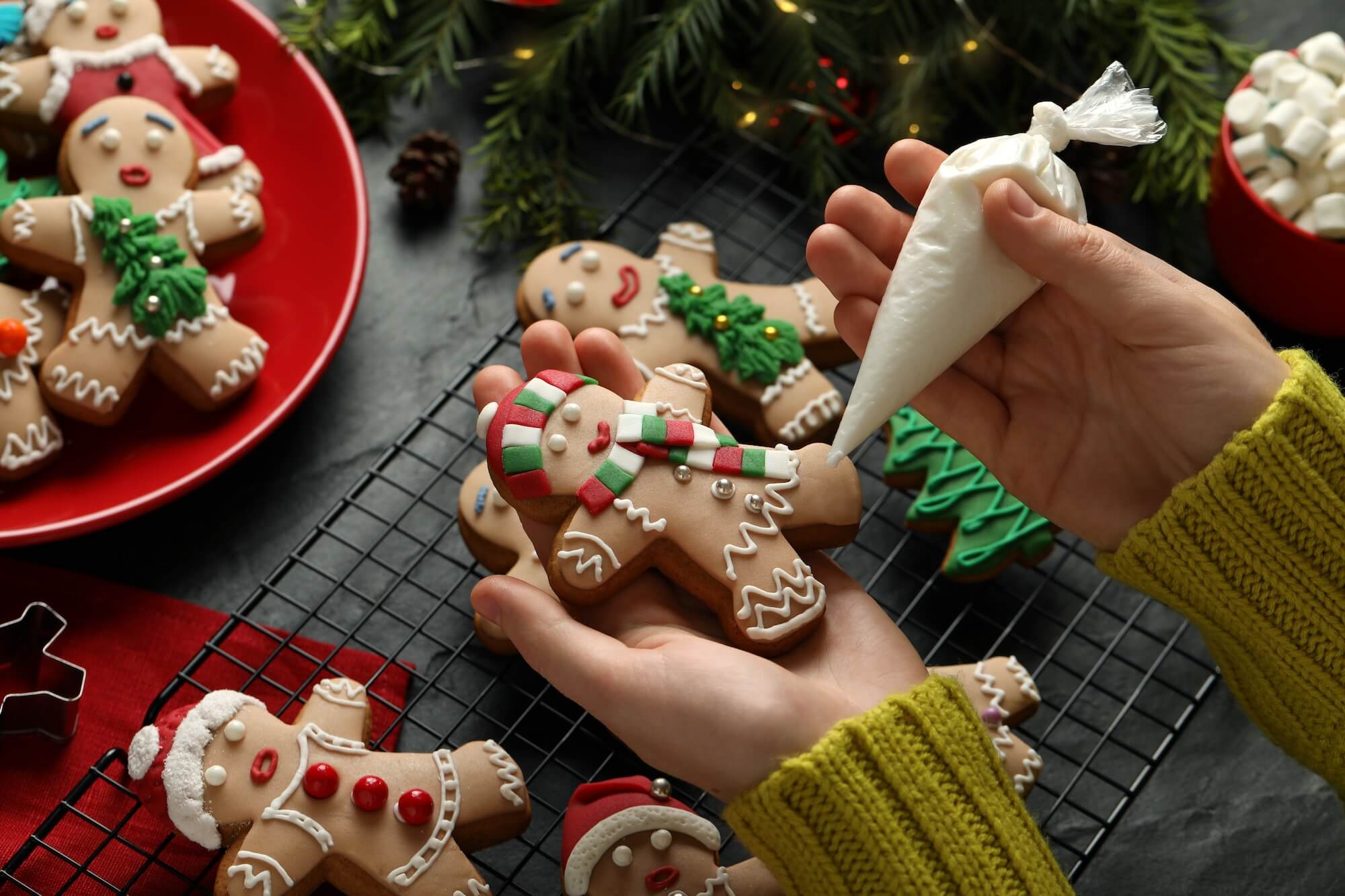 Person decorating gingerbread cookies with icing on a festive background