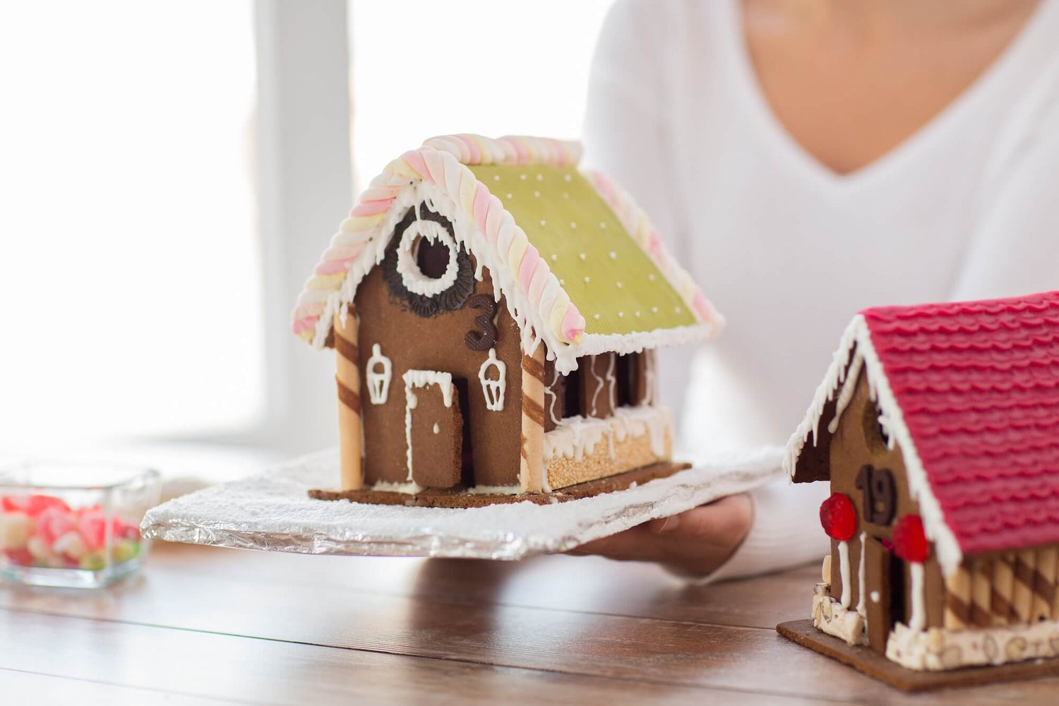 Two gingerbread houses on a table with a person in the background