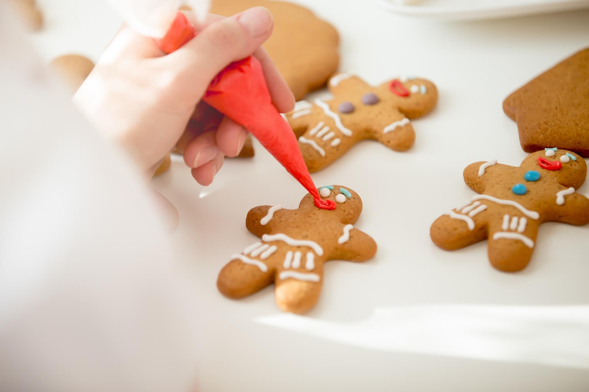Hand decorating gingerbread cookies with red icing on a white surface