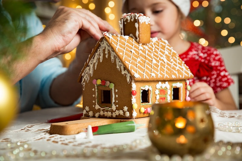 Two children decorating a gingerbread house with a blurred Christmas tree in the background