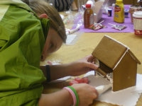 Person building a gingerbread house with various ingredients and tools on a table.
