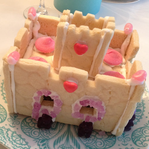 Small castle made of cookies with pink and red decorations on a decorative plate.