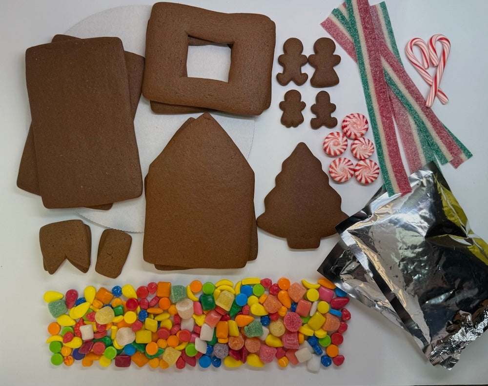 Gingerbread house kit with tree and gingerbread people, candy decorations, and icing on a white background.