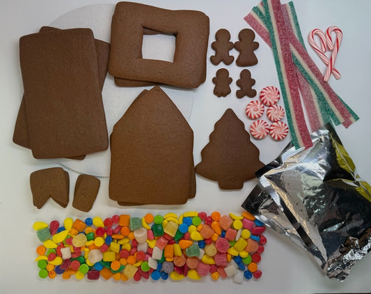 Gingerbread house kit with tree and gingerbread people, candy decorations, and icing on a white background.
