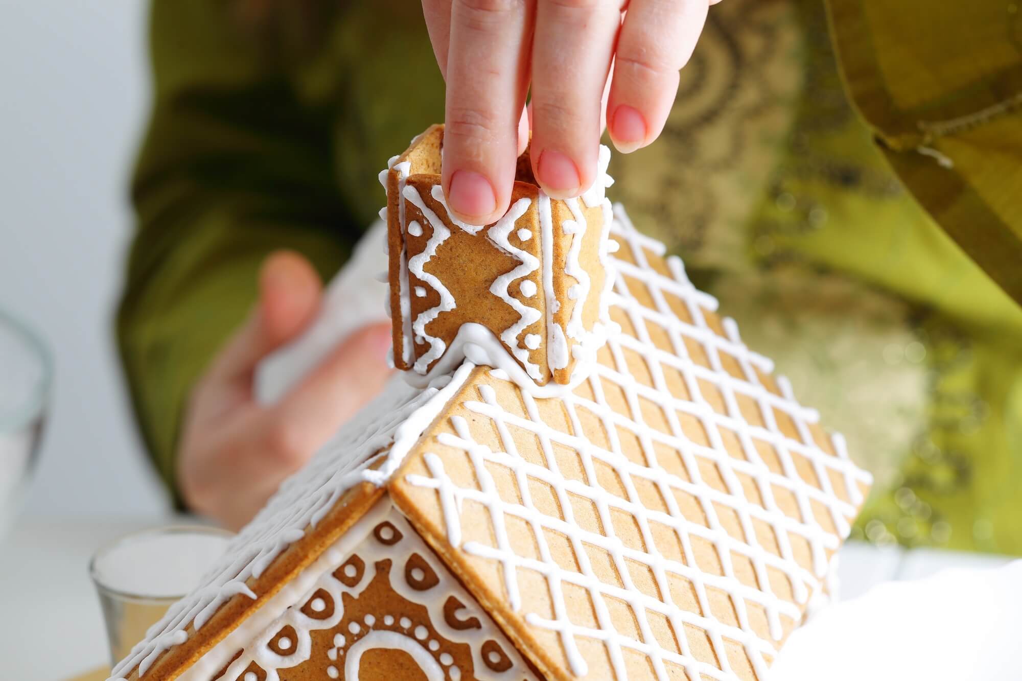 Decorating a gingerbread house with a hand placing a cookie on top.